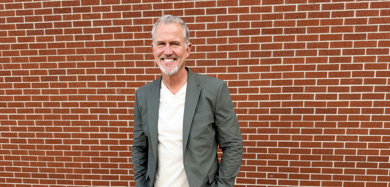 man in sports coat standing in front of a brick wall 